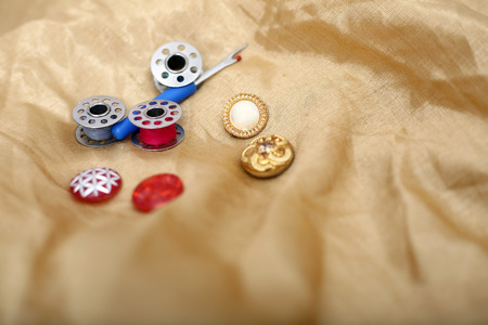 Portrait of needle ripper, button and bobbin on the golden cloth.