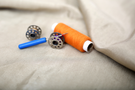 Photo of orange sewing thread, needle ripper and two bobbin on the cloth.の写真素材