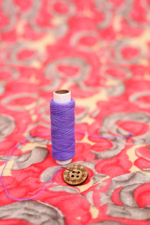 Portrait of purple thread and button. Isolated on the colorful background.