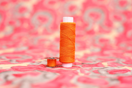 Portrait of sewing thread, bobbin and button. Isolated on the colorful background.