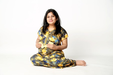 Portrait of pregnant lady is holding baby socks in hand with smile face and sitting on the floor. Isolated on the white background.の写真素材