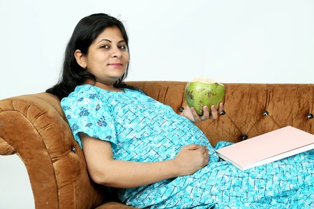 Pregnant lady is holding coconut water  with baby magazine.  Isolated on the white background.の写真素材
