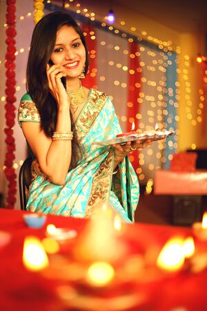Portrait of a beautiful young Indian woman in traditional dress celebrating diwali festival with in...