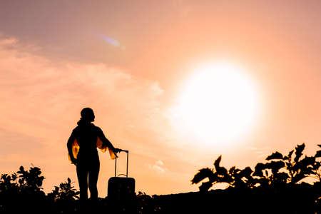 Silhouette of a woman with a suitcase against the backdrop of the sunの写真素材
