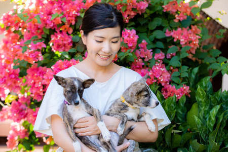 A Japanese woman holding two cute puppies in a colorful garden