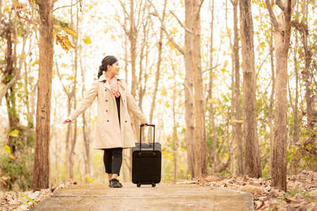 A woman walking along the road with a black suitcaseの写真素材