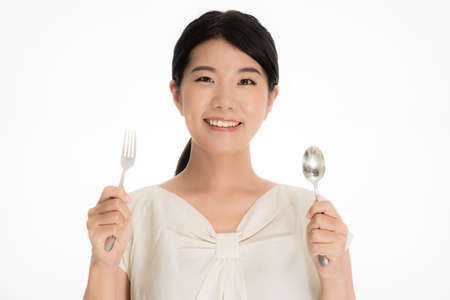 Smiling young Japanese woman with fork and spoonの写真素材