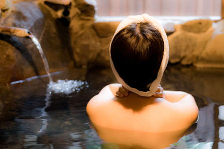 Japanese woman bathing in hot spring made of rockの写真素材