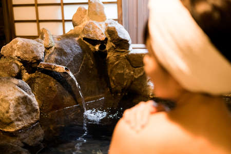 Japanese woman bathing in hot spring made of rockの写真素材