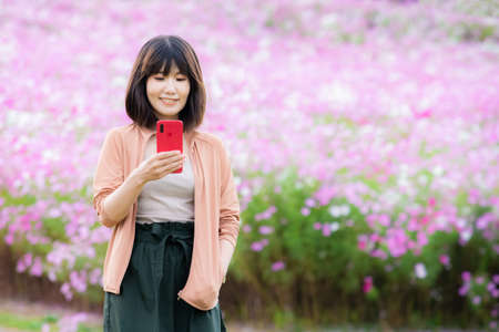 Woman holding smartphone in pink flower gardenの写真素材