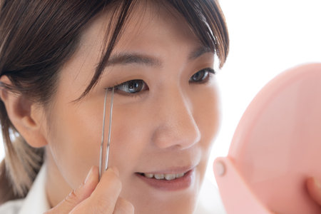 young asian woman using tweezers to check her face skinの写真素材