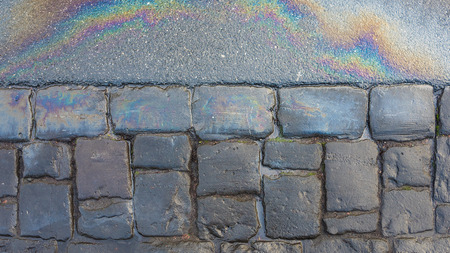 rainbow colors created by spilt oil or fuel on a roadside with a bluestone edgeの写真素材