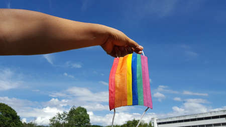 Hands hold a colorful mask with blue background. A concept is for pride month and encourage LGBTQIA communities around the globe.の写真素材