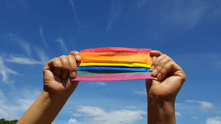 A colorful mask is holding in a hand with blue background, a concept for pride month and encourage LGBTQIA communities around the globe.の写真素材