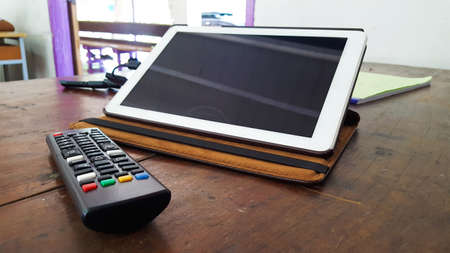 Tablet and black tv remote with its faded buttons in a classroomの写真素材