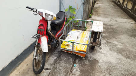 A traditional homemade motorbike with sidecar is parked near a houseの写真素材
