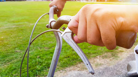 Hands are on a vintage bike handle which the break shaft tip is broken, the handle is at closed to the green field, the sunlight shines on a handの写真素材