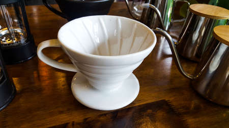 The white pottery coffee cup with the handle on the marbleize wooden floor surrounding by glass and silver shining kettlesの写真素材