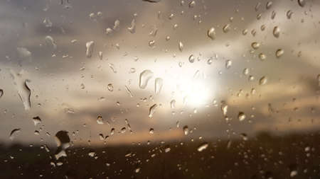 The rainwater drops cover the car window with storm clouds and the evening sunlight in backgroundの写真素材