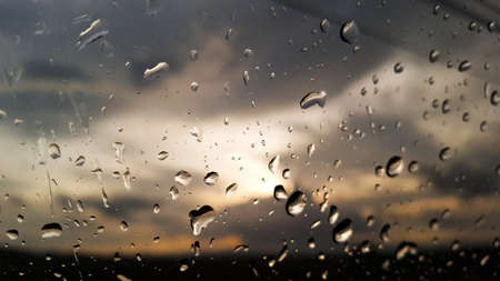 The rainwater drops cover the car window with storm clouds and the evening sunlight in backgroundの写真素材