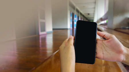 Smart phone hold in hands with blur brown porch and bench of building in background, concept of using technology device to contact parentsの写真素材