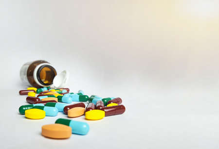 Various medicine pills, orange tablets, blue and green capsules pouring out of the brown bottle,...