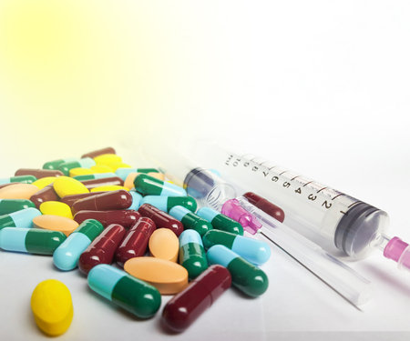 Various medicine pills, orange tablets, blue and green capsules, and injection syringe on white background, soft and selective focusの写真素材
