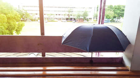 A dark blue umbrella on the wooden bench edited with the sun light and a building in backgroundの写真素材