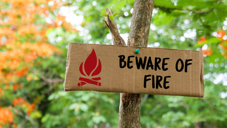 Brown paper label with drawing of bonfire and the text beware of fire on tree trunk with blurred background in camping siteの写真素材