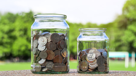 Coins in glass jar with blurred green trees background, concept of money savingsの写真素材