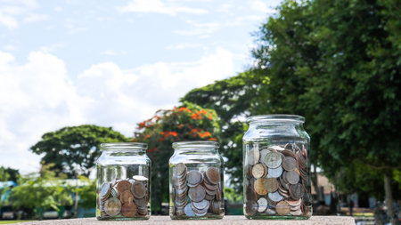 Coins in glass jar with blurred green trees background, concept of money savingsの写真素材