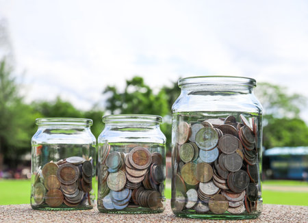 Coins in glass jar with blurred green trees background, concept of money savingsの写真素材