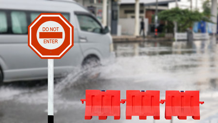 Red traffic sign with graphic of warning do not enter due to flood and red road barriers on blurred flooded street backgroundの写真素材