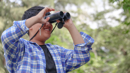 Young Asian boy is using a binocular to lookout for birds and animals in a local park, soft and selective focusの写真素材