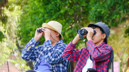 Young Asian boys are using a binocular to lookout for birds and animals in a local park, soft and selective focusの写真素材