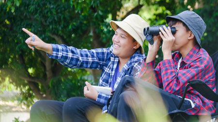 Young Asian boys are using a binocular to lookout for birds and animals in a local park, soft and selective focusの写真素材