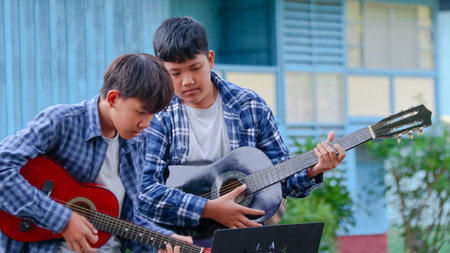 Young boys are playing acoustic guitars in front of a house, soft and selective focusの写真素材