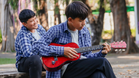 Young Asian boys are playing acoustic guitars in front of a house, soft and selective focusの写真素材