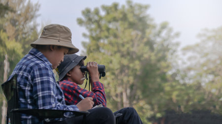 Young Asian boys are using a binocular to lookout for birds and animals in a local park, soft and selective focusの写真素材