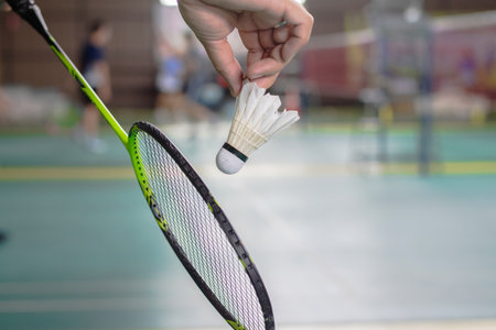 The badminton player holding a white shuttlecock and racket and standing at the net ready to serve.の写真素材