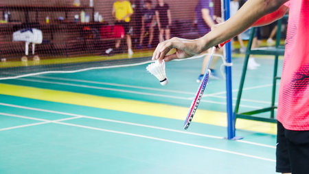 The badminton player holding a white shuttlecock and racket and standing at the net ready to serve.の写真素材