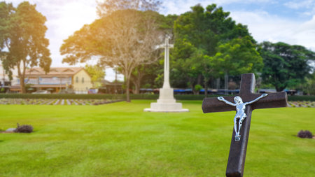 A red wooden cross on a blurred cemetery background. The wooden cross stands prominently, symbolizing peace and remembrance. The blurred gravestones in the background create a serene and solemn atmosphere.の写真素材
