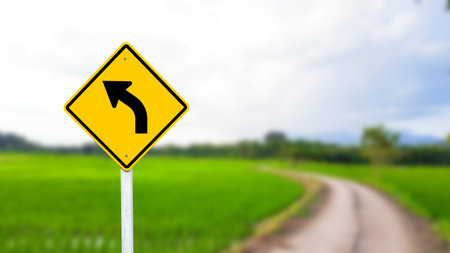 A black left-curved arrow is displayed on a bright yellow sign. The bold arrow indicates a left turn ahead, ensuring drivers are aware of the upcoming change in direction. The vivid yellow background enhances visibility for safe navigation.の写真素材