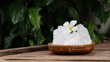 A basket filled with white alum crystals sits on a vibrant green shrub background. The contrasting colors highlight the purity of the alum against the lush greenery, creating fresh feeling.の写真素材