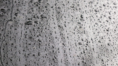 This image captures raindrops on a dark surface, highlighting their glistening clarity and natural beauty. The droplets and the dark background emphasizes refreshing essence of rain.の写真素材
