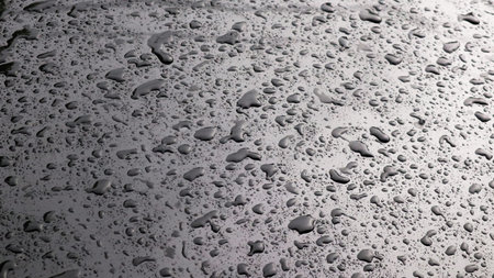 This image captures raindrops on a dark surface, highlighting their glistening clarity and natural beauty. The droplets and the dark background emphasizes refreshing essence of rain.の写真素材
