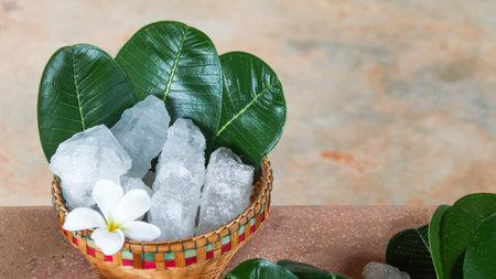 A basket filled with white alum crystals sits on a vibrant green shrub background. The contrasting colors highlight the purity of the alum against the lush greenery, creating fresh feeling.の写真素材