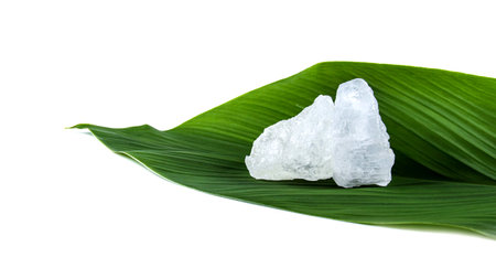 White crystal clear alum cube on green leaf isolated on white background. The chemical compound substance concept of spa and beauty industry.の写真素材