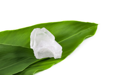 White crystal clear alum cube on green leaf isolated on white background. The chemical compound...