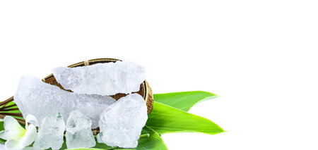 White crystal clear alum cube on green leaf isolated on white background. The chemical compound...